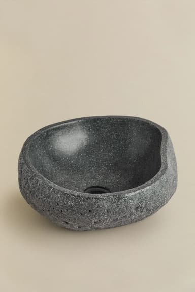 A vessel sink with an irregular, organic shape resembling a natural stone or boulder. The exterior features a rough, textured finish with visible pores, while the interior is smooth and concave, designed to hold water. A drainage hole is present at the bottom center of the interior basin. — 3D model
