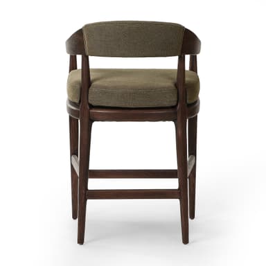 A bar stool with a wooden frame and upholstered seat and backrest. The frame is constructed from dark wood with visible grain. The seat and backrest are upholstered in a textured, olive-green fabric. The stool has a curved backrest that extends to armrests, and its legs are supported by crossbars. — 3D model