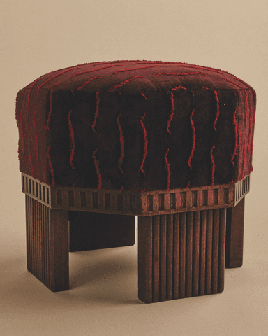 An Art Deco style upholstered stool featuring a hexagonal top with rich, deep red fabric that has a contrasting lighter red textured, wavy pattern. The stool is supported by a dark wooden base with a distinctive frieze of rectangular cutouts just below the upholstery, transitioning to fluted or reeded vertical panels that form the legs. — 3D model