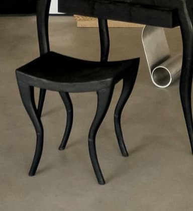 A single, matte black molded plastic chair with gracefully curved legs and a contoured backrest. The chair exhibits a seamless construction, with an open back design that integrates the backrest into the seat structure. Its sleek, minimalist form suggests a modern aesthetic. — 3D model