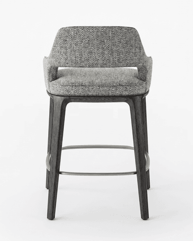 A modern bar stool with a fabric-upholstered seat and backrest, supported by dark-stained wooden legs. The stool features a curved back and armrests integrated into the main body. A metal footrest connects the four legs. — 3D model