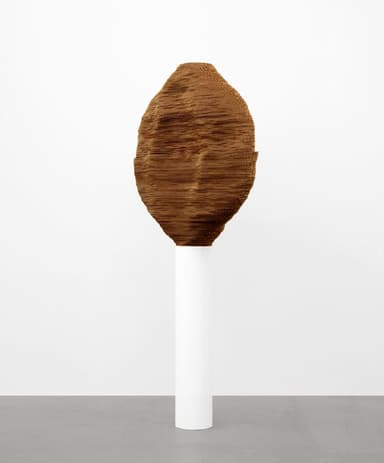 A large, irregularly shaped abstract sculpture with a textured, woven surface in a rich brown hue, displayed prominently on a tall, minimalist white cylindrical pedestal. — 3D model
