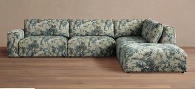 A sectional sofa with a corner chaise lounge. The sofa features a densely patterned upholstery with a botanical motif in shades of blue, green, and beige. It has a low profile with visible dark feet. — 3D model