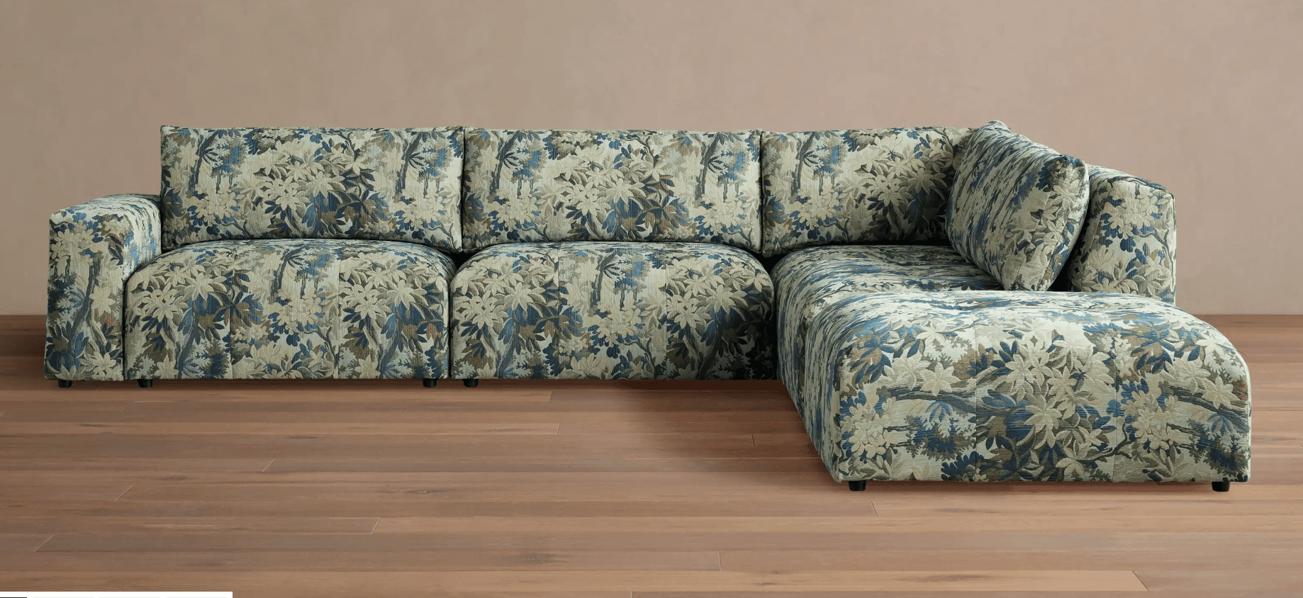 A sectional sofa with a corner chaise lounge. The sofa features a densely patterned upholstery with a botanical motif in shades of blue, green, and beige. It has a low profile with visible dark feet. — 3D model