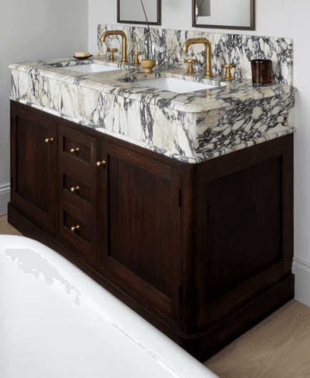 A double sink bathroom vanity with a marble countertop and wooden base. The vanity features two undermount sinks, brass faucets, and a backsplash. The base is constructed from dark wood and includes two cabinet doors and three drawers, all fitted with brass knobs. — 3D model