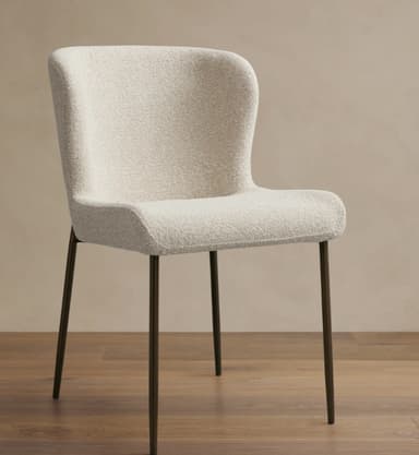 An armless dining chair featuring a gently curved, high backrest and seat, fully upholstered in a textured cream-colored boucle fabric, supported by four slender, dark metal tapered legs. — 3D model