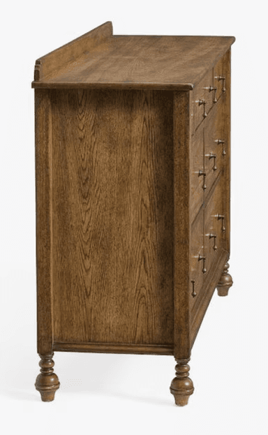 A wooden dresser with multiple drawers. It features a top surface with a raised edge, and a series of drawers of varying sizes arranged in a grid. The drawers are equipped with simple, metallic pull handles. The dresser stands on four turned legs, with the front legs having a more decorative, bulbous shape. — 3D model
