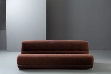 A compact, armless loveseat upholstered in a textured, dark reddish-brown fabric, featuring a minimalist design with a chrome-finished metal bar accent along the base. — 3D model