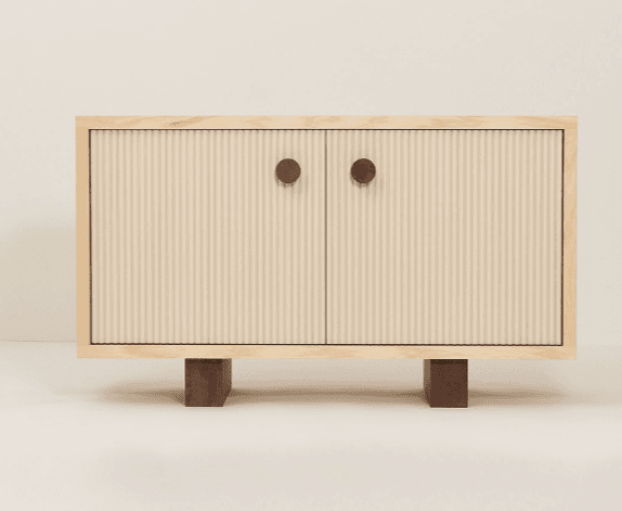 A cabinet with two doors and a light wood frame. The doors have a ribbed texture and are adorned with two round, dark brown knobs. The cabinet stands on two short, rectangular wooden legs with a dark brown finish. — 3D model