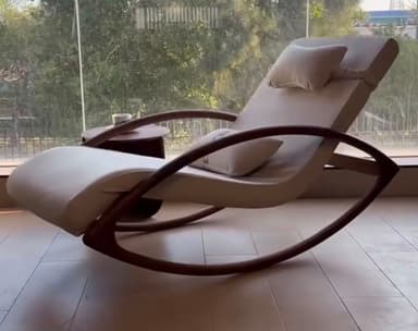 A modern rocking chaise lounge featuring a contoured, padded seat upholstered in a light cream or off-white fabric or faux leather, supported by a distinctive curved dark wood or bentwood frame that functions as both structural support and rocking runners. It includes an integrated, adjustable headrest pillow and an additional lumbar cushion, both matching the main upholstery. — 3D model