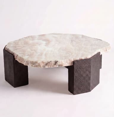 A low-profile coffee table featuring a thick, organically shaped tabletop made from light-colored onyx with natural veining and rough, unpolished edges. The top rests upon four substantial, rectangular block legs made of a dark, textured material, possibly cast metal or resin, giving the table a robust and earthy aesthetic. — 3D model