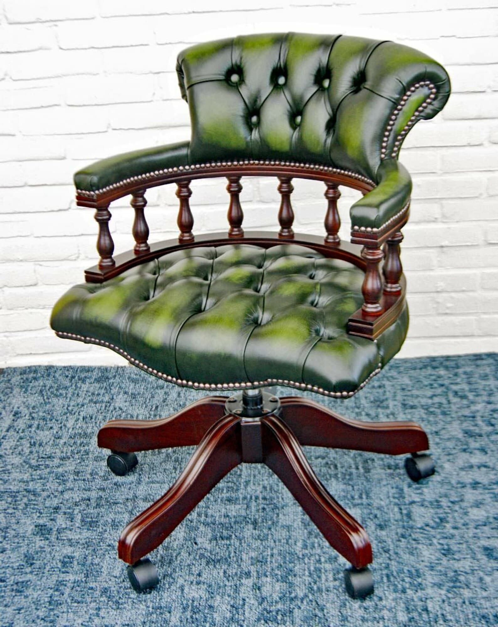 A classic green leather office chair featuring a deep tufted back and seat, traditional turned wooden armrests, and a dark wood five-star swivel base with casters. The leather has a slightly distressed, antique appearance, accented with decorative nailhead trim along the edges of the upholstery and armrests. — 3D model