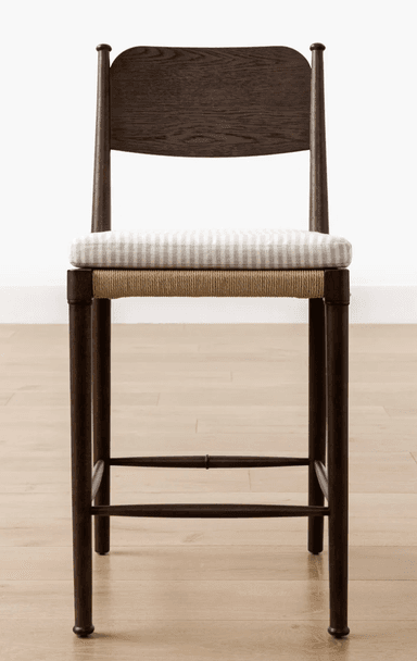 A contemporary bar stool featuring a dark wood frame, a woven rope seat base, and a removable upholstered cushion with a light stripe pattern. It includes a contoured wooden backrest and four tapered legs with integrated footrest rungs. — 3D model