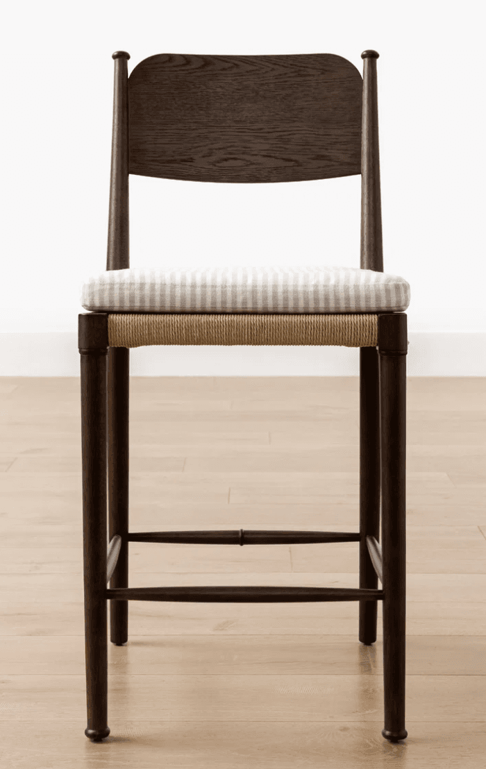 A contemporary bar stool featuring a dark wood frame, a woven rope seat base, and a removable upholstered cushion with a light stripe pattern. It includes a contoured wooden backrest and four tapered legs with integrated footrest rungs. — 3D model