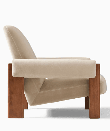 A single armchair with a wooden frame and upholstered cushioning. The armchair has a reclined backrest, wide armrests, and a seat cushion. The wooden frame appears to be constructed from solid wood with a warm brown finish, forming the legs and structural supports. The upholstery is a light beige or cream color, with a soft texture visible. — 3D model