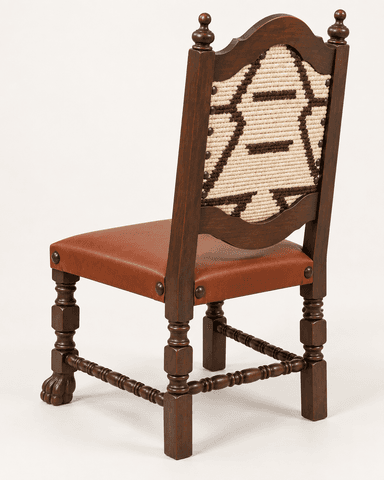 A dark stained wooden side chair in a Spanish Colonial Revival style, featuring a reddish-brown leather upholstered seat and a decorative woven textile back panel. The chair has elaborately turned legs, including one front leg with a distinctive paw or claw foot. The seat and back panel are secured with dark metal nailhead trim. The back posts are topped with turned finials, and the backrest has a shaped top rail. Spindle stretchers connect the legs. — 3D model