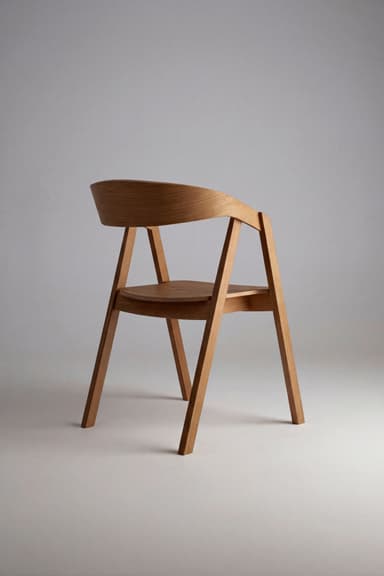 A modern armchair constructed from light-toned wood, featuring a curved backrest that flows into integrated armrests. The seat is an upholstered pad covered in a light grey textured fabric. — 3D model
