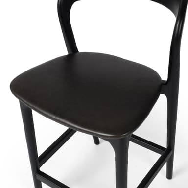 A contemporary bar stool with a black wooden frame and a dark upholstered seat. The stool features a gently curved backrest and a square footrest connecting the tapered legs. — 3D model