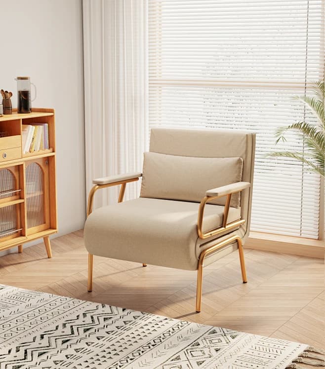 A modern armchair featuring a beige upholstered body, gold-colored tubular metal frame, and a matching lumbar pillow. — 3D model