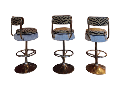A high-backed swivel bar stool featuring a circular seat and curved backrest upholstered in a distinctive tiger print fabric. The seat edge is adorned with a white or silver fringe. The stool is supported by a polished brass-finished pedestal base with a trumpet-shaped bottom and a circular footrest, allowing for swivel functionality. — 3D model