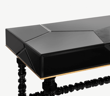 A rectangular console table featuring a glossy black finish with a segmented, geometric top surface. The apron beneath the top has a gold-toned trim. The table is supported by four ornately turned black legs, connected by similarly turned stretchers. The legs terminate in brass-colored feet. — 3D model