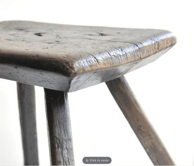 A rustic wooden stool with a square seat and three legs. The seat is flat with rounded edges and shows signs of wear, including some visible imperfections and grain texture. The legs are cylindrical and tapering slightly towards the bottom, appearing to be hand-shaped. The overall aesthetic suggests a primitive or country style. — 3D model
