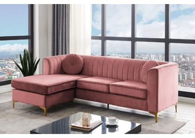 A modern L-shaped sectional sofa upholstered in blush pink velvet fabric, featuring a right-hand facing chaise lounge and distinctive vertical channel tufting on its backrest and arms. It is supported by slender, gold-finished metal legs and includes two round accent pillows. — 3D model