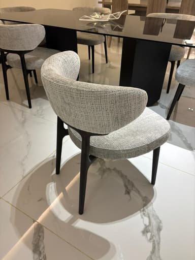 A modern upholstered chair with a curved backrest and a seat. The chair has four tapered legs and appears to be made of wood or metal with a dark finish. The upholstery is a textured fabric in a neutral tone. — 3D model