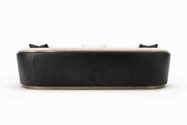 A contemporary curved sofa featuring a cream-colored boucle fabric upholstery. The sofa has a distinct curved silhouette and integrated armrests that are partially clad in dark, possibly black, leatherette or faux leather, framed by a brass or bronze-finished metal trim. A continuous metal trim also accents the base of the sofa. It comes with two black square throw pillows and two circular, cream-colored boucle pillows. — 3D model