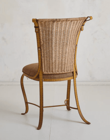 A vintage chair with a woven wicker back and a padded seat. The frame appears to be made of metal and is painted yellow with visible stitch-like detailing. The legs are curved and provide a decorative, elegant stance. The backrest has a distinctive shape, widening towards the top with curved accents. — 3D model