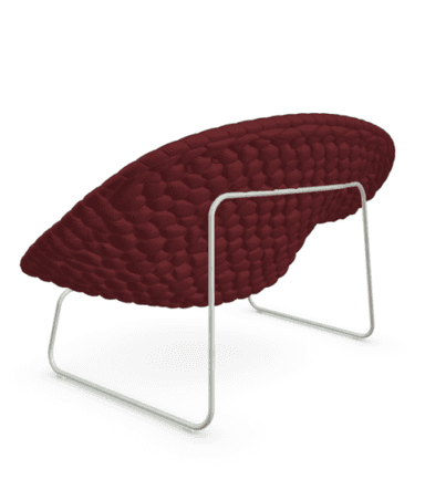 A modern lounge chair featuring a wide, scooped seating surface crafted from a deep maroon knitted or woven cord material, giving it a textured, sculptural appearance. The chair is supported by minimalist, light-colored metal wire frame legs. It includes a rectangular lumbar pillow in a complementary, slightly brighter red fabric. The overall design emphasizes comfort and a contemporary aesthetic. — 3D model