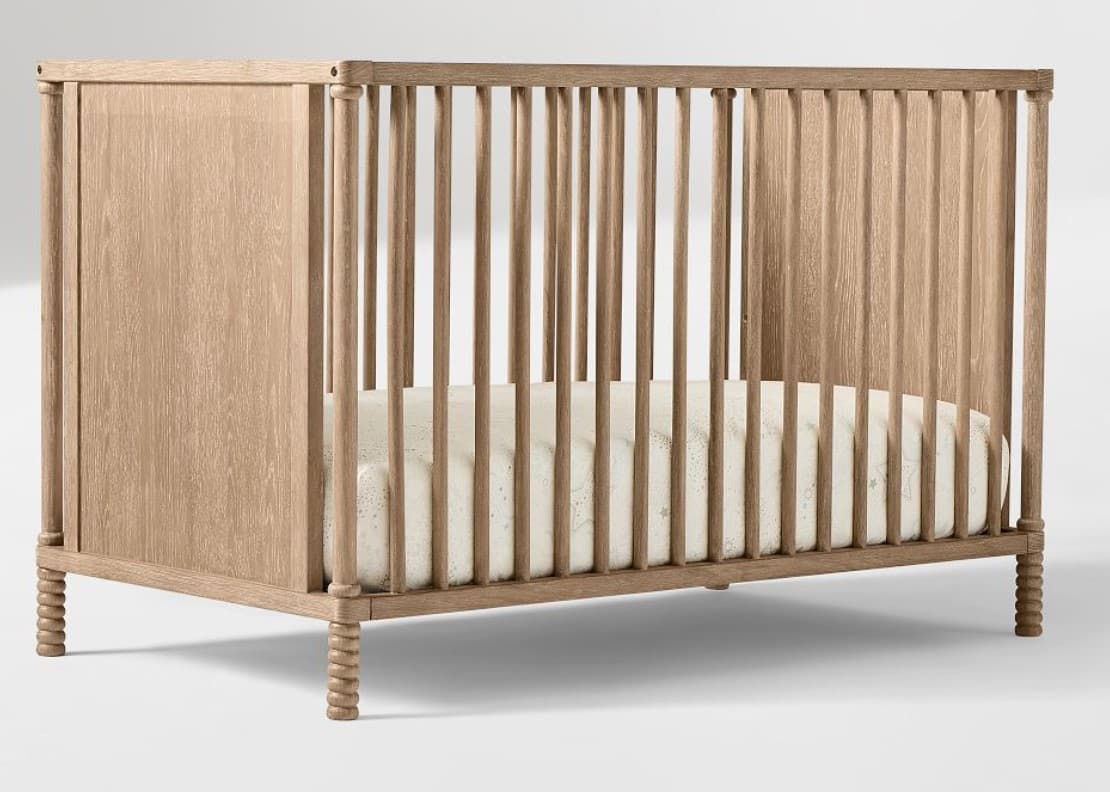 A wooden crib with slatted sides and a solid headboard/footboard. The crib has a mattress inside with a patterned cover. The legs are turned, providing a decorative detail. — 3D model