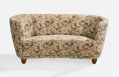 A vintage-style, curved sofa upholstered in a floral fabric with a pastel color palette. The sofa features a rounded backrest with vertical channeling and integrated armrests that curve inwards. It is supported by four short, tapered wooden legs. — 3D model