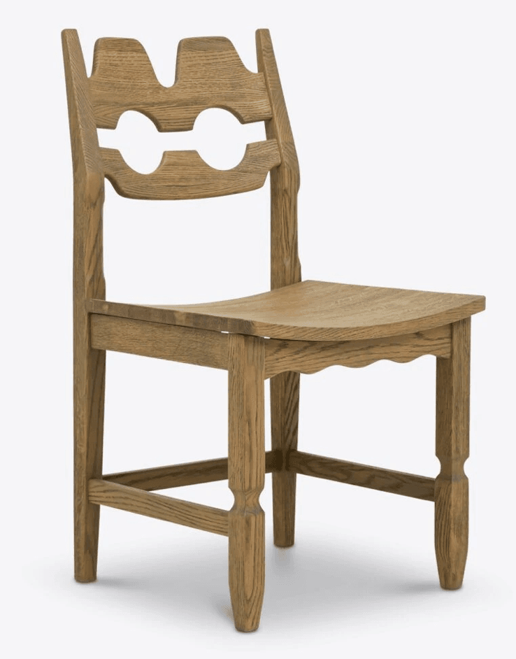 A wooden chair with a distinctively carved backrest featuring two circular cutouts and an abstract, crown-like top. The seat is subtly contoured for comfort. The legs are square-sectioned with decorative grooves and taper towards the feet. The overall design suggests a rustic or folk art influence. — 3D model