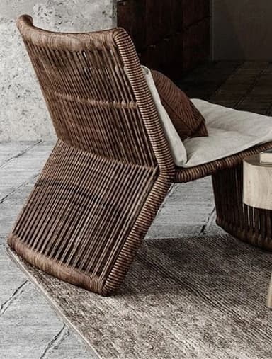 A modern lounge chair constructed from a woven material, featuring a sloping seat and back. It includes a light-colored seat cushion and a small, dark brown throw pillow with ribbed texture. — 3D model