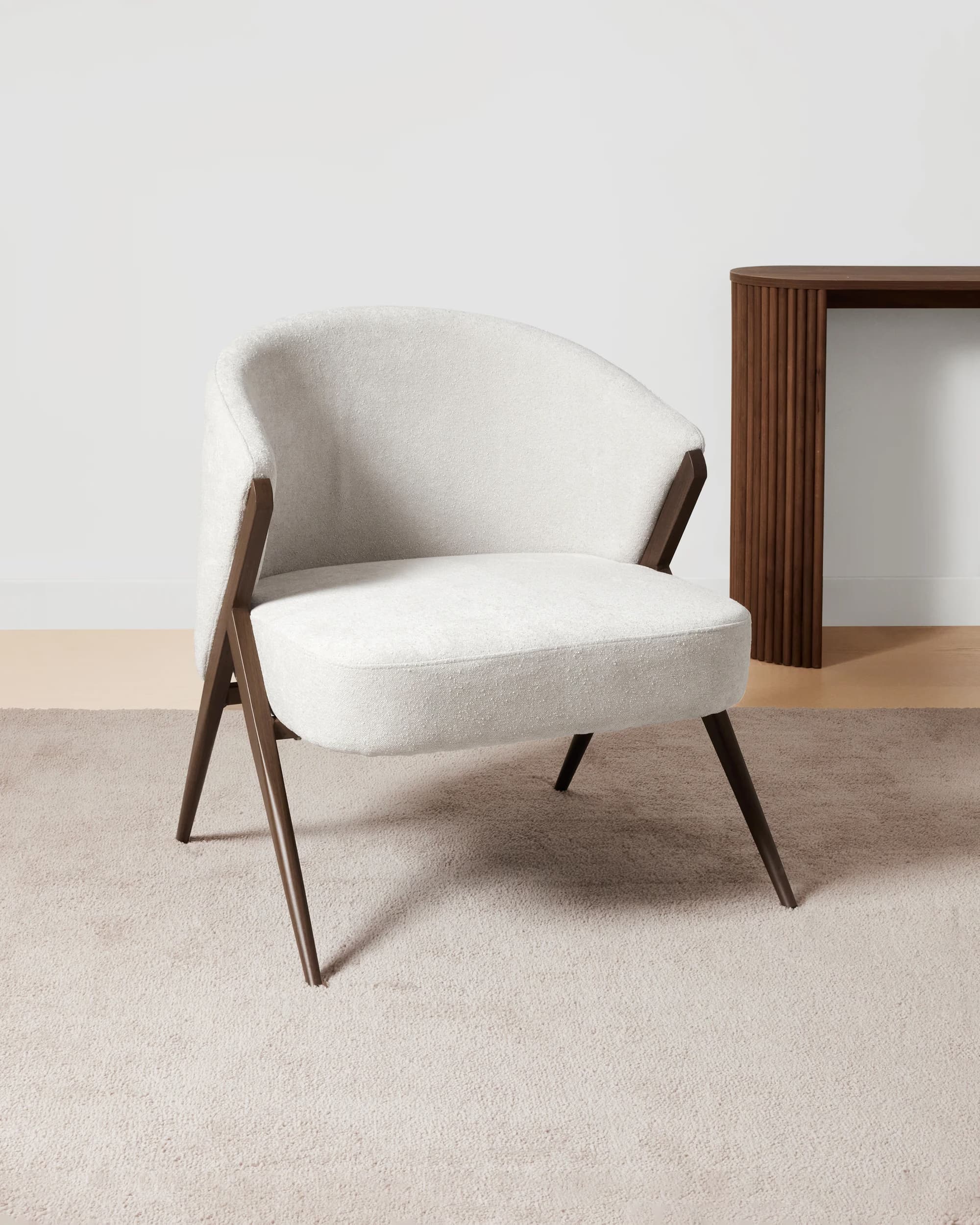 A modern armchair with a rounded back and seat, upholstered in a textured off-white fabric. The frame and legs are made of dark wood, featuring an angular, open design that supports the upholstered shell. — 3D model