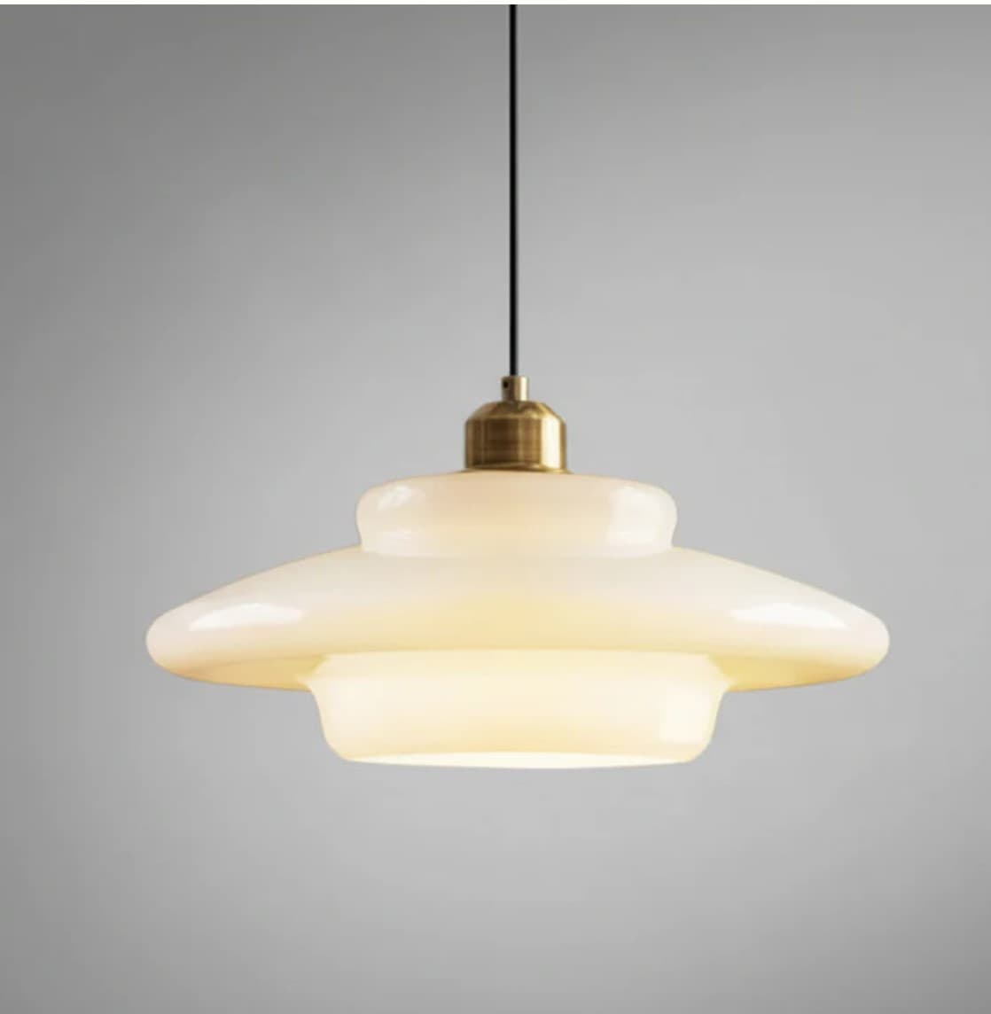 A contemporary pendant light featuring a layered opal glass shade suspended by a black cord with brass hardware. — 3D model