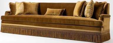 A large, rectangular sofa upholstered in golden-brown velvet fabric, featuring a full decorative fringe skirt around the base and multiple plush throw pillows. — 3D model