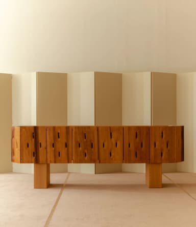 A long, low credenza with a unique, carved front featuring irregularly shaped cutouts. The piece rests on two thick, rectangular wooden legs. The top surface is smooth and appears to be a single, solid piece of wood. The overall design is modern with a natural, organic feel. — 3D model