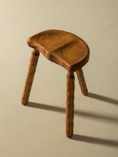 A three-legged wooden stool with an oval, contoured seat. The legs are carved with a textured pattern, giving them a rustic appearance. The overall design is simple and organic. — 3D model