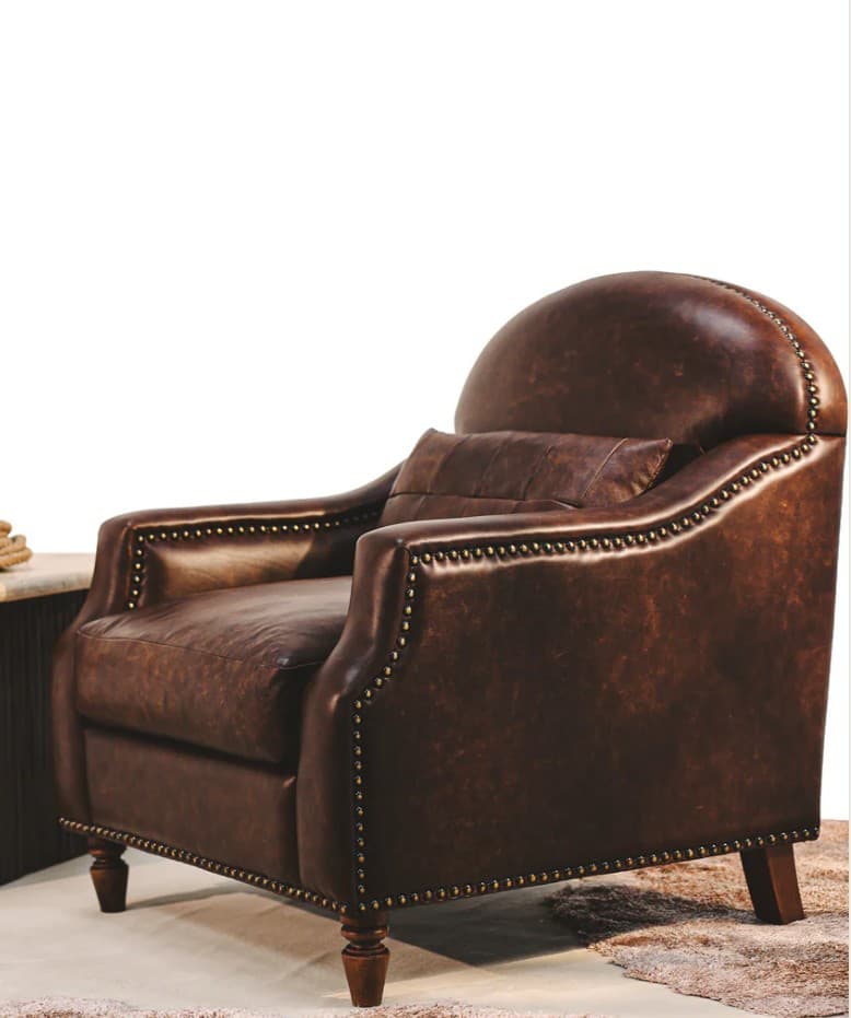 A vintage-style armchair upholstered in dark brown distressed leather. The chair features a high, rounded back, padded arms, and a single seat cushion. It is adorned with brass nailhead trim along the edges of the arms, back, and base. The chair rests on four turned wooden legs. — 3D model