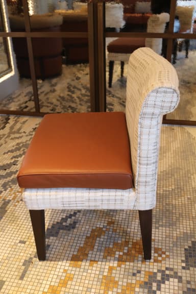 An armless dining chair featuring a light, patterned fabric upholstered back and frame, contrasted with a smooth, warm brown leather seat cushion. The chair stands on four dark, slightly tapered wooden legs. — 3D model