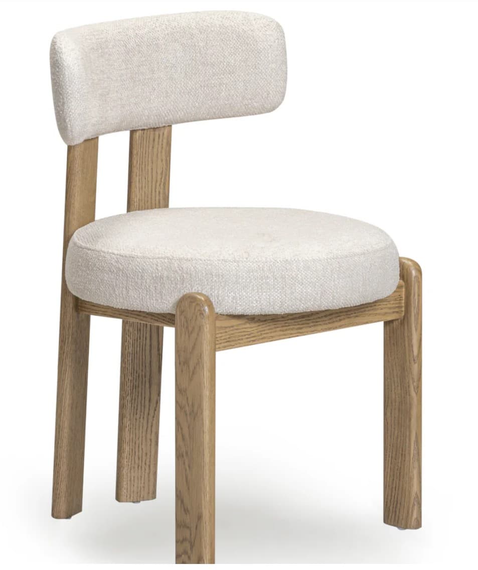 An armless dining chair featuring a light-toned solid wood frame and fully upholstered seat and backrest. The upholstery is a light beige or cream-colored fabric with a visible boucle-like texture. The chair design emphasizes soft curves, with a rounded backrest and seat, and legs that have subtly rounded edges. The construction appears sturdy and modern, suitable for dining or accent seating. — 3D model