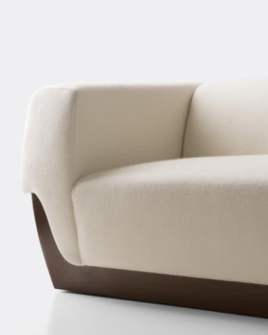 A close-up view of a segment of a modern sofa. The upholstery appears to be a textured fabric in an off-white or cream color. The base of the sofa is constructed from a dark wood, featuring a curved, minimalist design that supports the upholstered section. The contrast between the light fabric and the dark wood base is a prominent design feature. — 3D model
