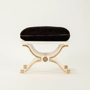 A white and gold X-base stool with a dark brown upholstered cushion, featuring classical design elements. — 3D model