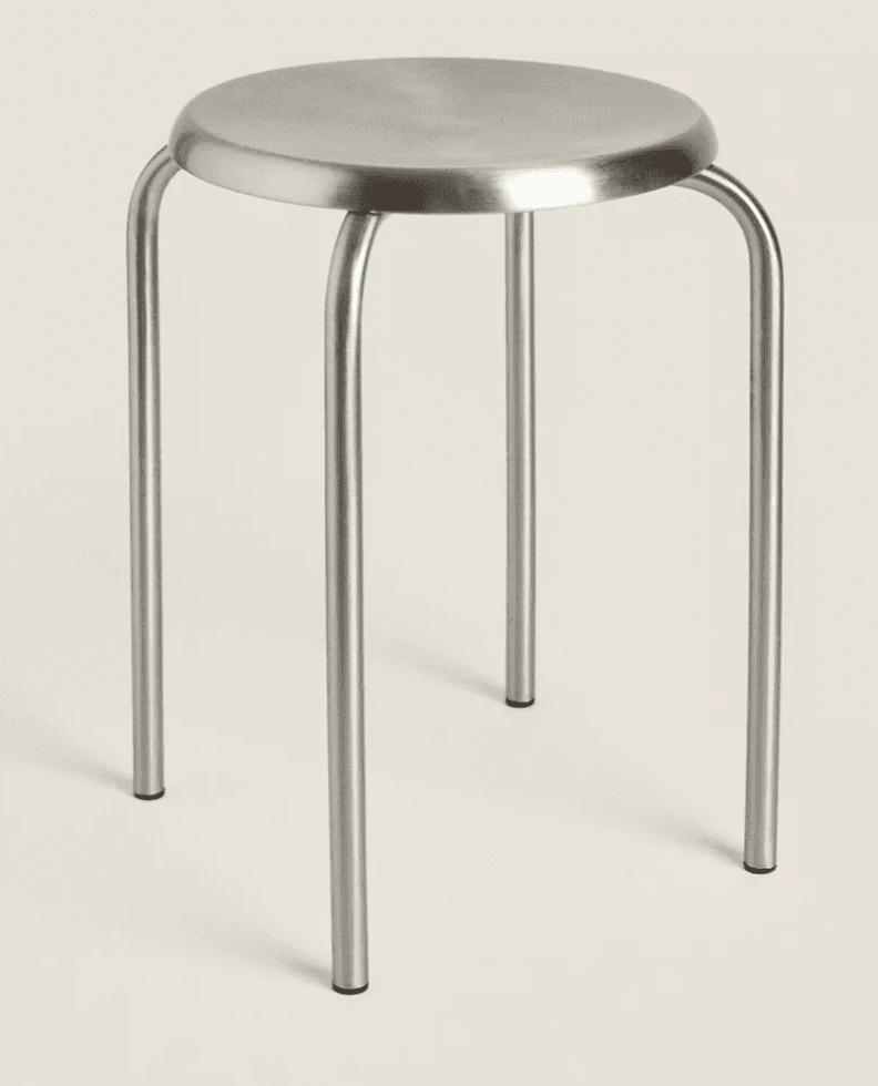 A minimalist, stackable stool featuring a round metal seat and four tubular metal legs. The entire stool has a brushed metallic finish, suggesting a robust and utilitarian design. — 3D model