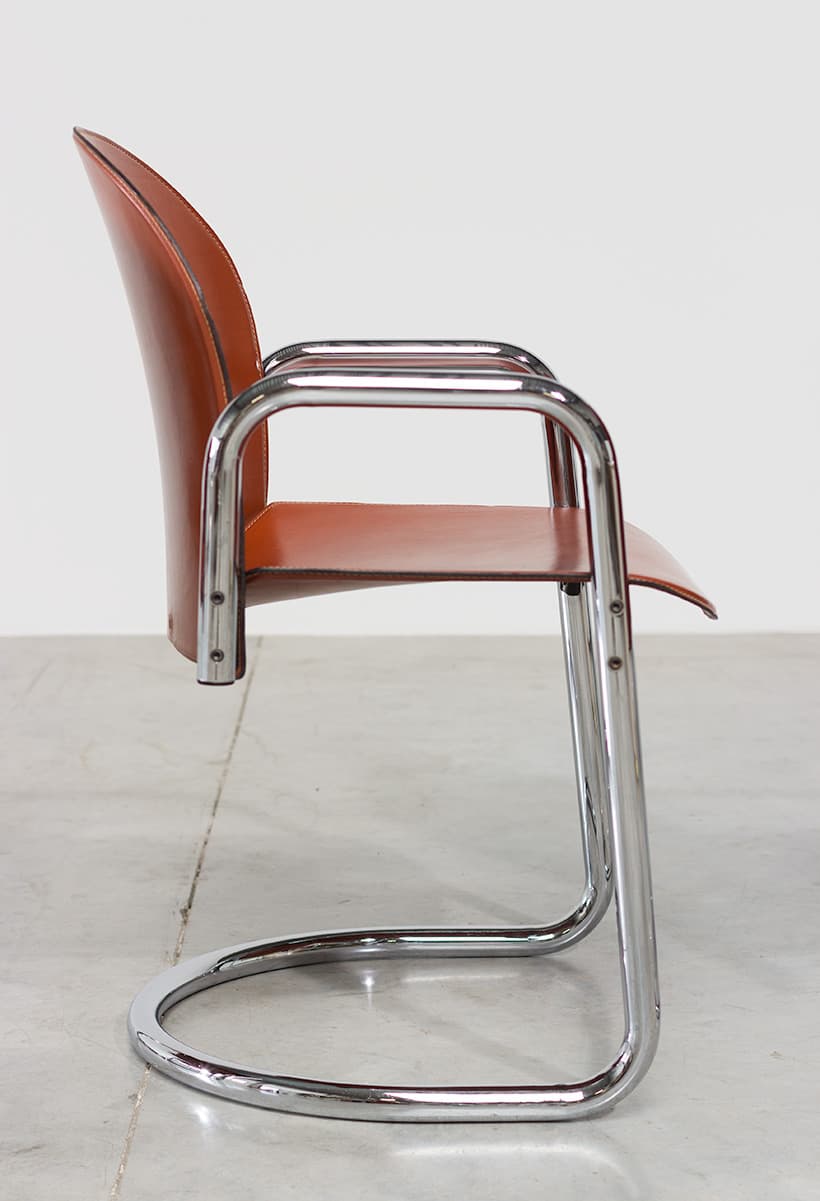A cantilever armchair with a chrome-plated tubular steel frame and a brown leather seat and backrest. The frame has a continuous curve forming the legs, seat support, and armrests. The backrest is slightly curved and extends upwards, with a visible seam running along its edge. The seat is a flat plane that connects to the frame. The overall design suggests a mid-century modern or Bauhaus influence. — 3D model