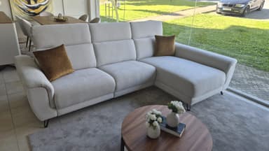 A modern, light-colored L-shaped sectional sofa featuring a chaise lounge extension and adjustable headrests. The sofa is upholstered in a textured fabric and includes two decorative throw pillows. It stands on minimal, dark-colored metal legs. — 3D model