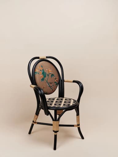An armchair featuring a black painted rattan or bentwood frame, an oval upholstered backrest with a detailed floral and bird pattern on a brown background, and a woven cane seat with a distinctive black and natural geometric pattern. The chair includes rattan-wrapped accents on the arms and legs, contributing to its eclectic bistro-inspired aesthetic. — 3D model
