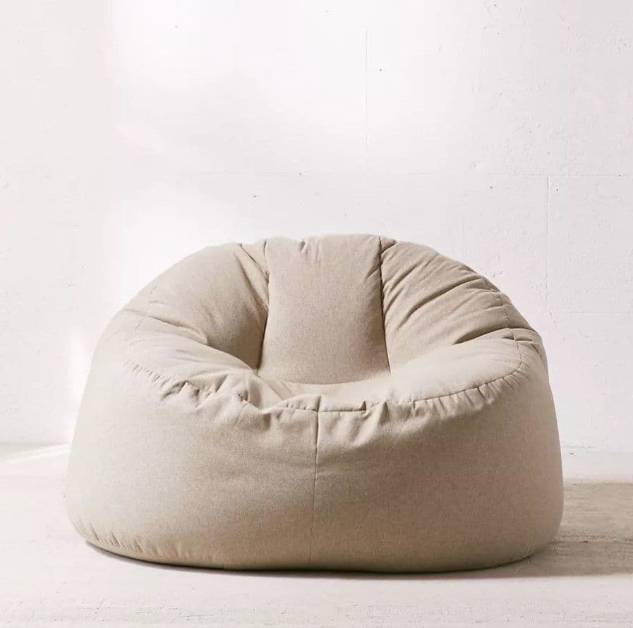 A single modern bean bag chair with a smooth, soft textile covering in a light beige or off-white color. The chair has a typical pear-like or teardrop shape, designed to conform to the user's body. It appears plump and well-filled, with subtle folds indicating the flexible nature of its construction. The simple design emphasizes comfort and casual seating. — 3D model
